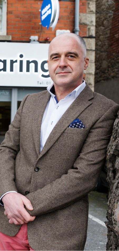Hidden Hearing expert audiologist Enda Dooley in a suit standing in front of Hidden Hearing Ballsbridge smiling