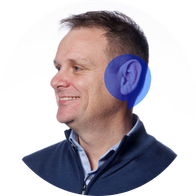 A photograph of Hidden Hearing audiologist David Lyons smiling with a blue speech bubble overlayed on his ear