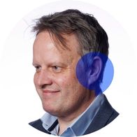 Hearing aid audiologist David Walsh smiling with a blue Hidden Hearing logo overlayed on his ear