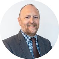 A headshot of Hidden Hearing audiologist Fergal Stynes smiling in a suit