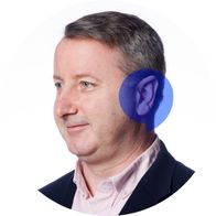 Hearing aid audiologist Jonathan Mooney smiling with a blue Hidden Hearing speech bubble overlayed on his ear