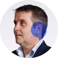 A photograph of hearing aid audiologist Noel Doherty smiling with a blue speech bubble overlayed over his ear