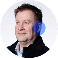 A headshot of Hidden Hearing hearing aid audiologist Tim Eacrett smiling with a blue speech bubble overlayed on his ear