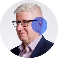 A photograph of hearing aid audiologist Tony Johnson smiling with a blue speech bubble overlayed over his ear