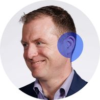 A photograph of hearing aid audiologist David Glennon smiling in a suit with a blue speech bubble overlayed over his ear