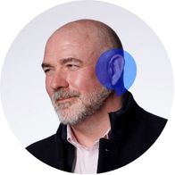 A picture of Audiologist Mark Kemp smiling with a blue speech bubble over his ear