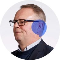 Clinic Coordinator Jason Byrne wearing glasses and posing for a photograph with a blue speech bubble overlayed on his ear