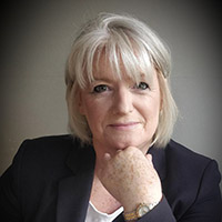 A senior individual with short gray hair rests their hand under their chin, seated in a neutral indoor setting. The face is blurred, obscuring identity. No hearing aids or text are visible.