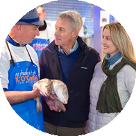 Couple interacting with fishmonger holding fresh fish at a fish market