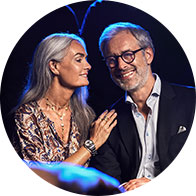 Woman with gray hair softly speaking into man's ear while seated closely together.