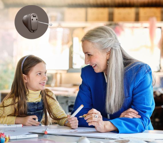 Woman in a blue blazer laughing while drawing with her granddaughter with a discreet hearing aid in her ear