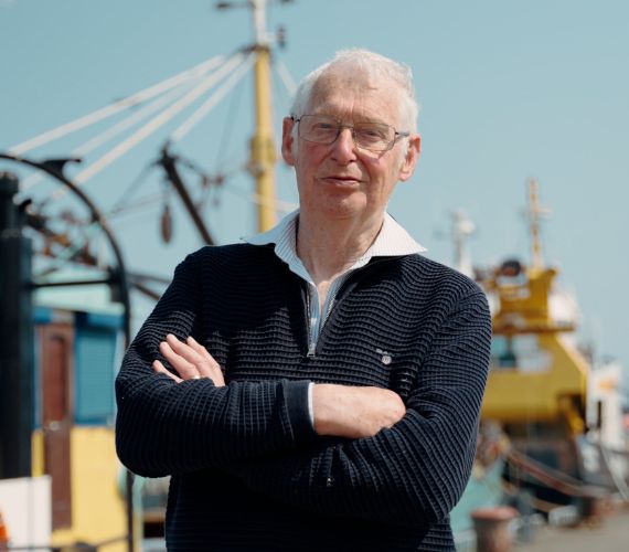 Older man looking satisfied while standing with his arms crossed with boats behind him