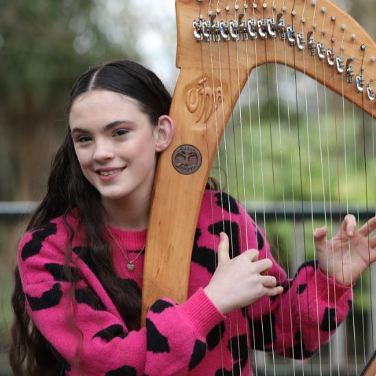 Hidden Hearing customer Una Walsh posing next to her harp while wearing her hearing aids