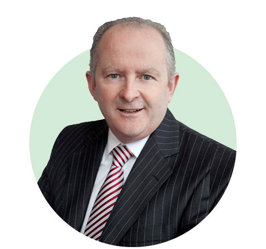 A person wearing a pinstriped suit, white shirt, and red striped tie is positioned against a light green circular background. The individual’s face is intentionally blurred for privacy. No text is visible.