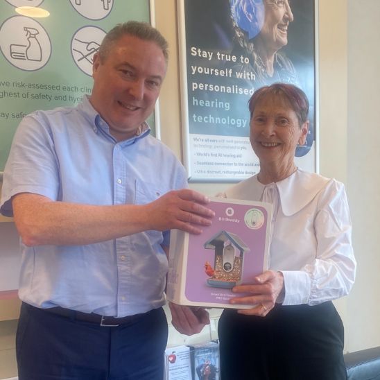 Picture of a Hidden Hearing audiologist giving a Bird Buddy Smart Camera Bird Feeder to a competition winner