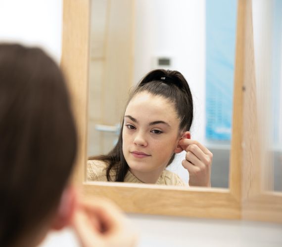 Photograph of a young girl with black hair putting in her state-of-the-art bluetooth hearing aids