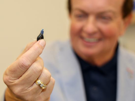A slightly out of focus Marty Morrissey smiling while holding an Oticon Zeal hearing aid