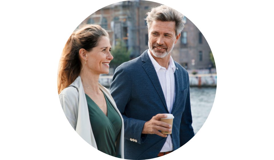 Man holding a coffee cup while walking outdoors near water with a woman.