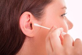 Close-up side view of a person inserting a cotton swab (Q-tip) into their ear while cleaning it.