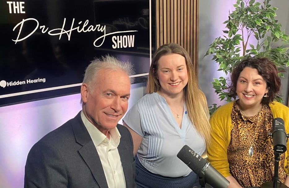 Dr Hilary hosting The Dr Hilary Show with Hidden Hearing branding visible.