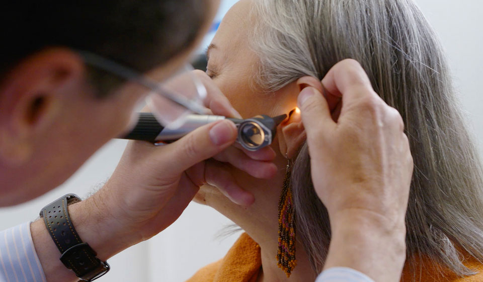Hearing specialist examining an older woman's ear with an otoscope.
