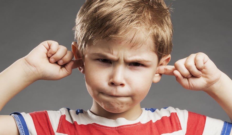 Child covering ears with fingers, wearing a striped shirt against a neutral background.