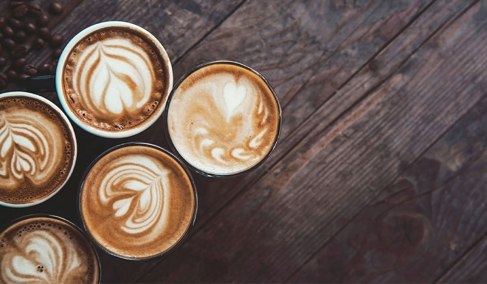 Latte art designs on coffee cups arranged on a rustic wooden table.