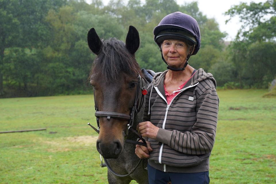 The alt description does not match the content of the image. A more optimized alt description for this image would be: Person wearing a helmet standing beside a brown horse in an outdoor field.