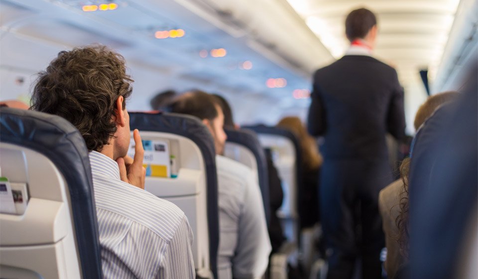 People seated inside an airplane cabin with a flight attendant walking down the aisle.