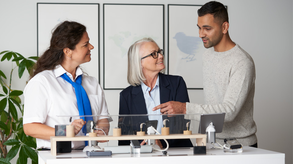 Hearing care specialists discussing hearing aid options with a customer in a clinic setting.