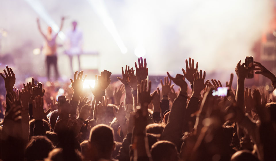 Audience with raised hands enjoying a live concert under bright stage lighting.