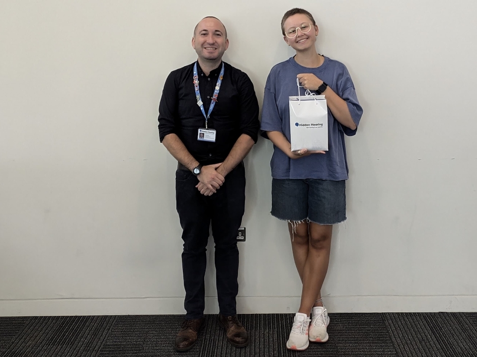 Hidden Hearing Give Back Program recipient holding a branded gift bag while standing beside a staff member.