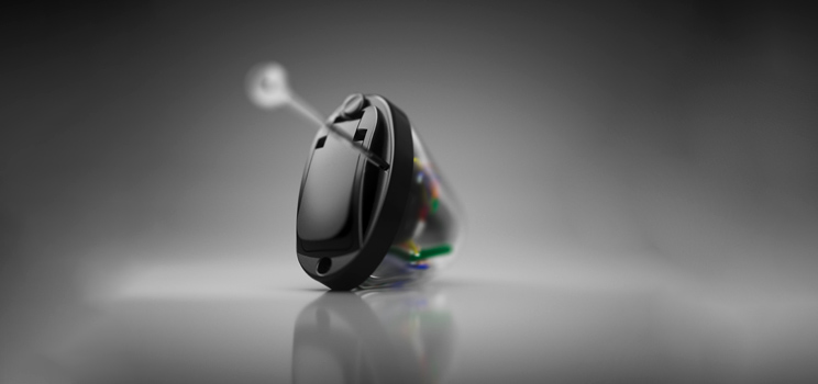 A sleek black in-the-ear hearing aid rests on a reflective surface, featuring intricate internal wiring. The device is set against a grayscale gradient background, emphasizing its modern, discreet design.