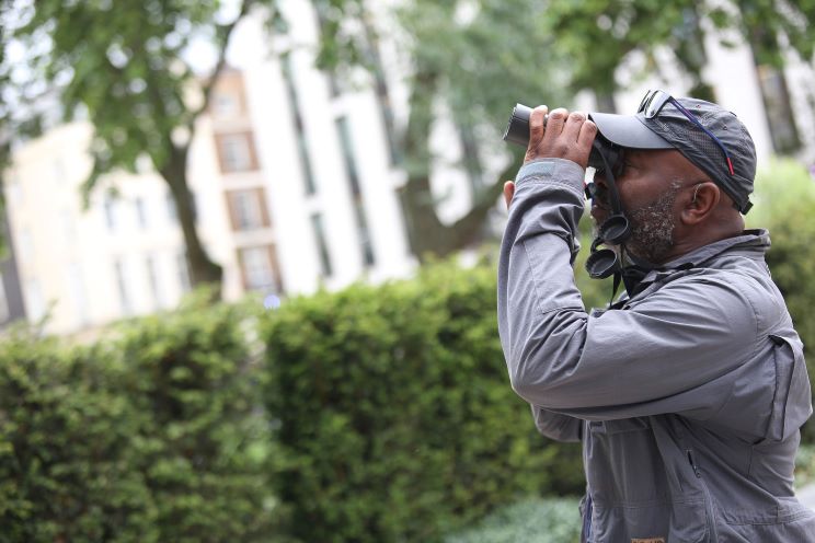 Person birdwatching in a park, promoting awareness of sound and hearing through Hidden Hearing's support of Dawn Chorus.