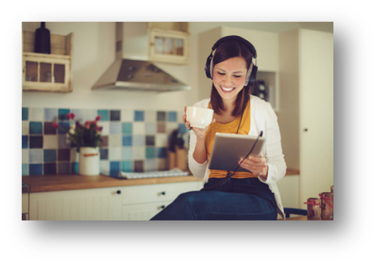 Woman wearing headphones in a kitchen, holding a cup and using a tablet.