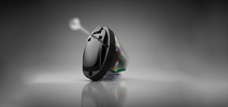 A sleek black in-the-ear hearing aid rests on a reflective surface, featuring intricate internal wiring. The device is set against a grayscale gradient background, emphasizing its modern, discreet design.