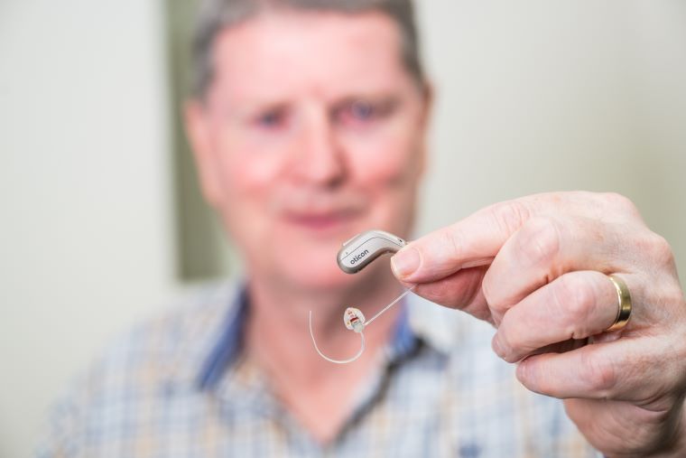 Tiny, discreet hearing aid held by a person wearing a plaid shirt.