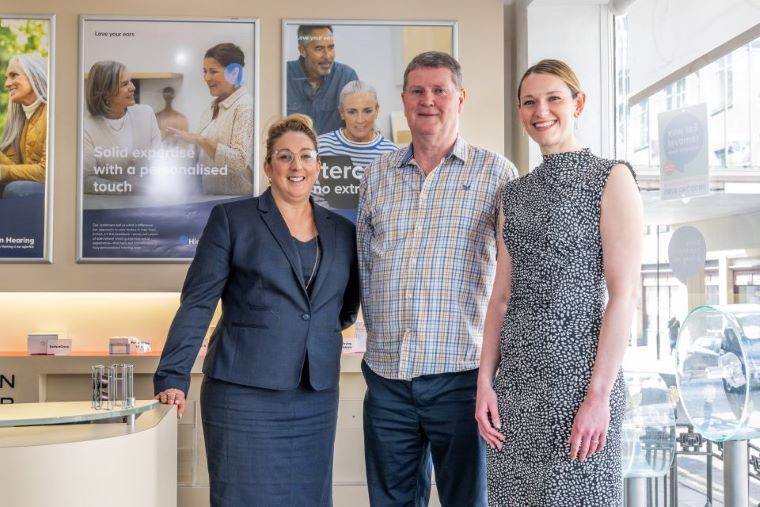 Hearing care specialists standing with a client in a modern clinic environment.