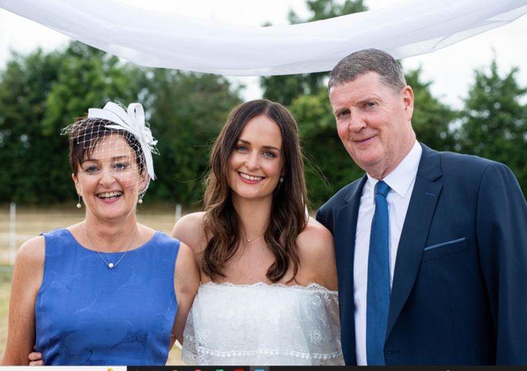 Family posing outdoors at a wedding ceremony under a white canopy, with greenery in the background.