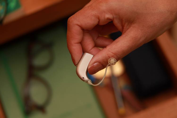 A hand holding a hearing aid with a drawer in background