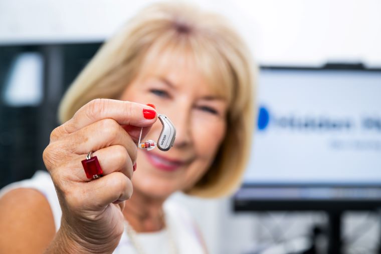 Jennie Bond showcasing a hearing aid from Hidden Hearing