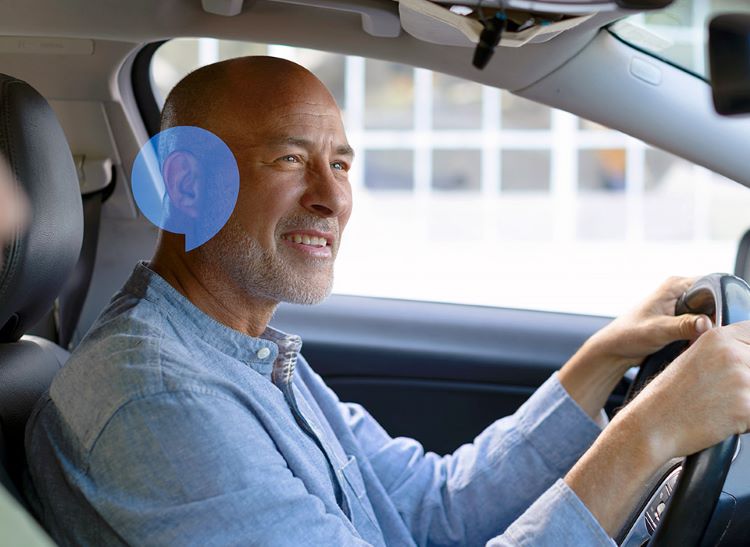 Man driving a car with a blue speech bubble near his right ear