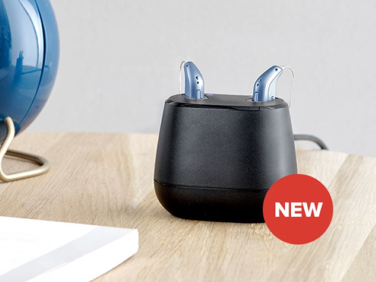 Oticon Intent hearing aids in a charging dock on a wooden surface.