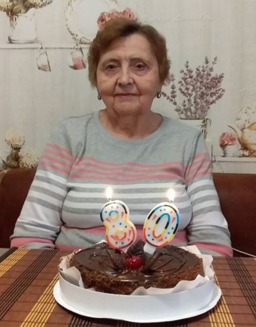 Elderly woman celebrating her 80th birthday with a chocolate cake topped with lit candles shaped as the number 80.