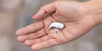 Invisible hearing aids placed on an open palm against a dark blue background.