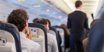 Man wearing hearing aids seated on an airplane with a flight attendant in the aisle.