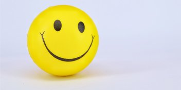 Yellow smiley face stress ball on a plain background, symbolizing happiness and positivity.