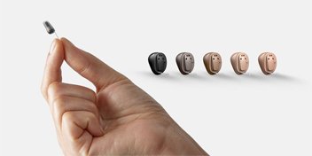 Range of hearing aids displayed, including a close-up of a discreet in-ear model held between fingers.