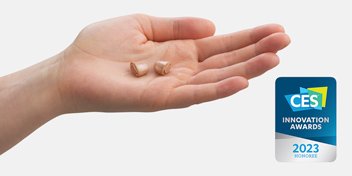 Custom in-the-ear hearing aids Oticon Own resting on an open palm, alongside a CES 2023 Innovation Awards Honoree badge.