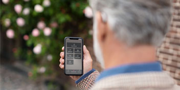 Man using iPhone to control Bluetooth hearing aids with garden background